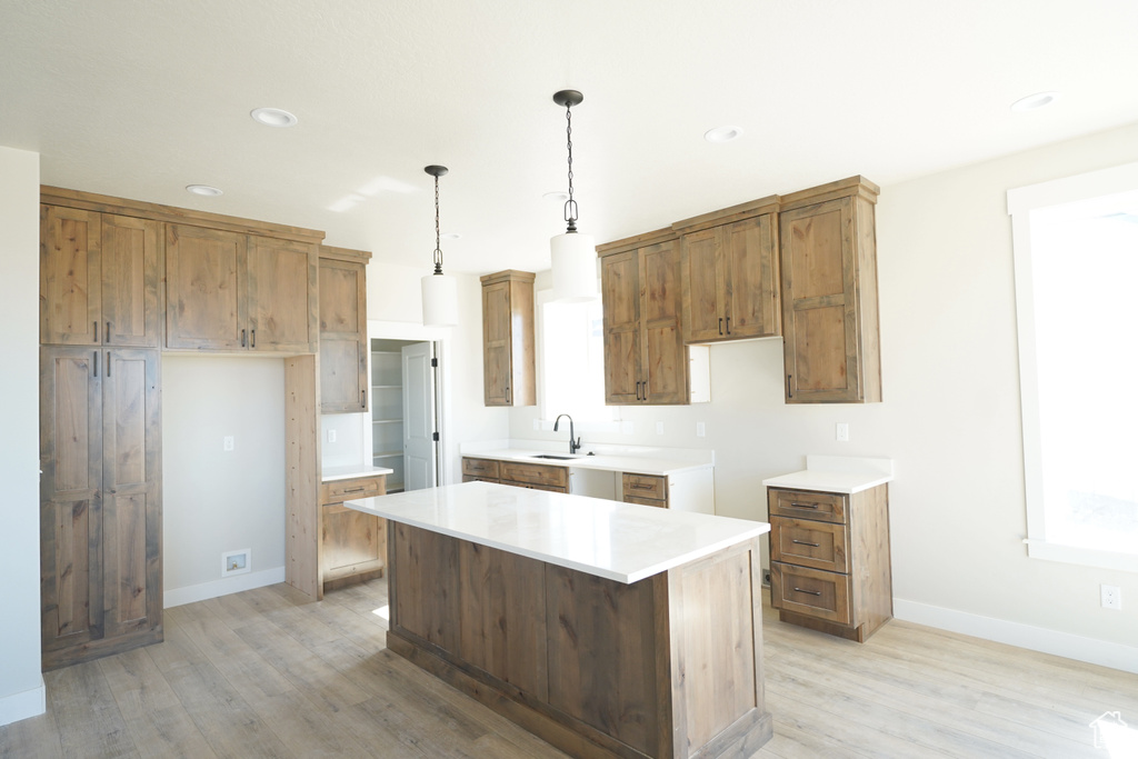 Kitchen with hanging light fixtures, light hardwood / wood-style floors, a kitchen island, and sink