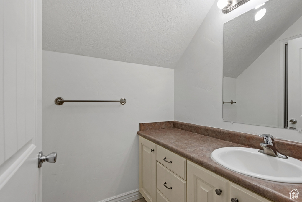 Bathroom with a textured ceiling, vanity, and lofted ceiling