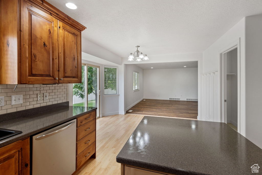 Kitchen featuring an inviting chandelier, hanging light fixtures, decorative backsplash, light wood-type flooring, and dishwasher