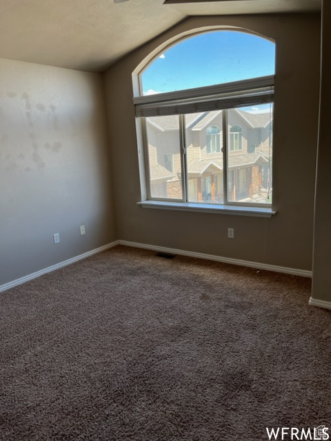 Carpeted spare room featuring vaulted ceiling