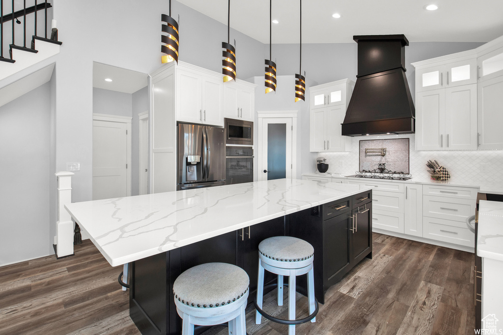 Kitchen featuring custom range hood, dark hardwood / wood-style floors, a kitchen island, appliances with stainless steel finishes, and backsplash