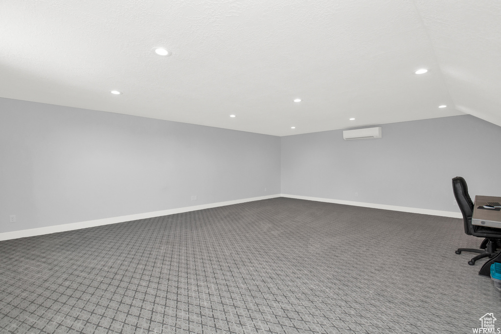 Unfurnished office featuring a wall mounted air conditioner, lofted ceiling, and carpet flooring