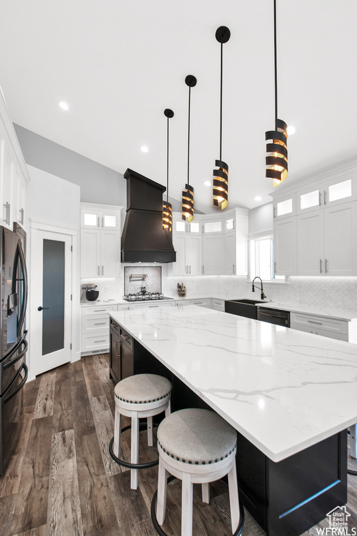 Kitchen with black appliances, decorative light fixtures, decorative backsplash, a spacious island, and custom range hood