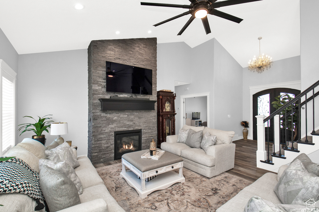 Living room with hardwood / wood-style flooring, vaulted ceiling, ceiling fan with notable chandelier, and a fireplace