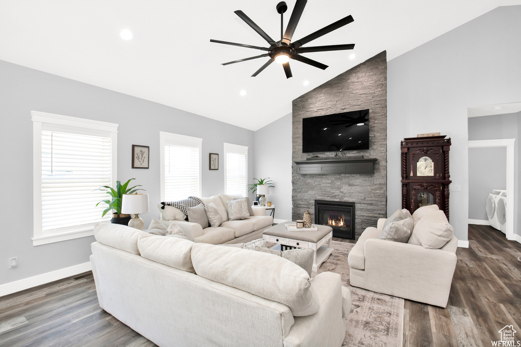 Living room with independent washer and dryer, ceiling fan, dark hardwood / wood-style floors, a stone fireplace, and high vaulted ceiling