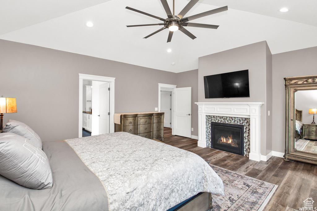 Bedroom featuring lofted ceiling, dark wood-type flooring, ceiling fan, a tile fireplace, and ensuite bath