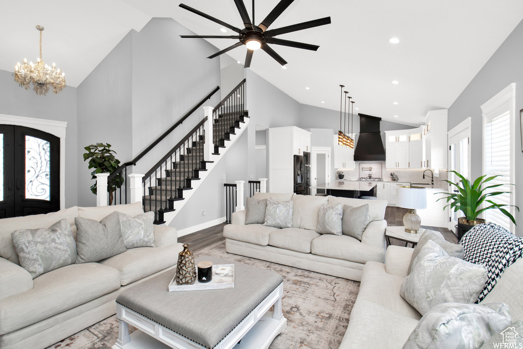 Living room with high vaulted ceiling, ceiling fan with notable chandelier, french doors, and light hardwood / wood-style flooring