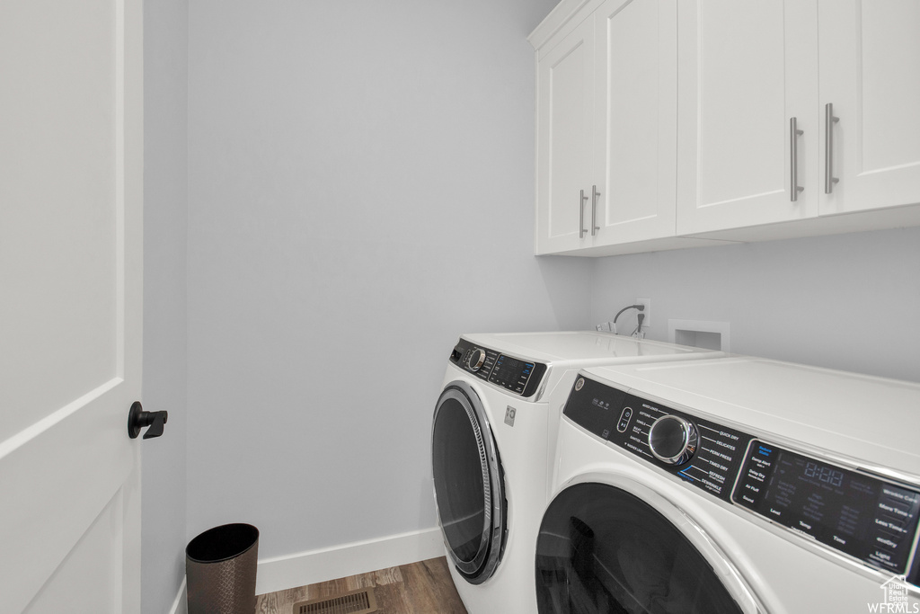 Clothes washing area with washing machine and dryer, dark hardwood / wood-style flooring, and cabinets