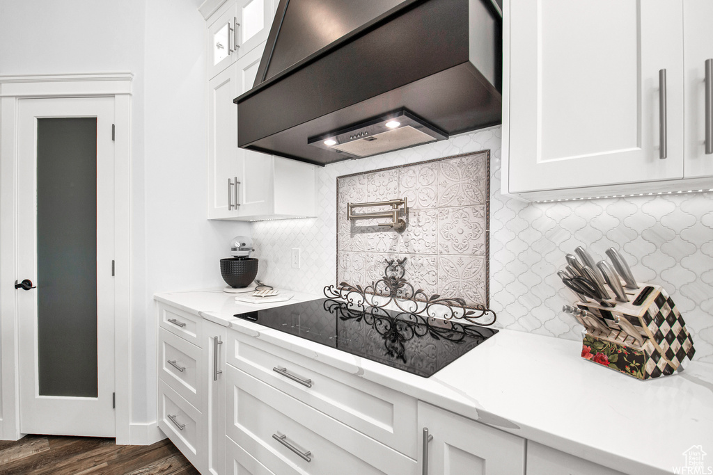 Kitchen with black electric stovetop, white cabinetry, premium range hood, decorative backsplash, and dark hardwood / wood-style floors