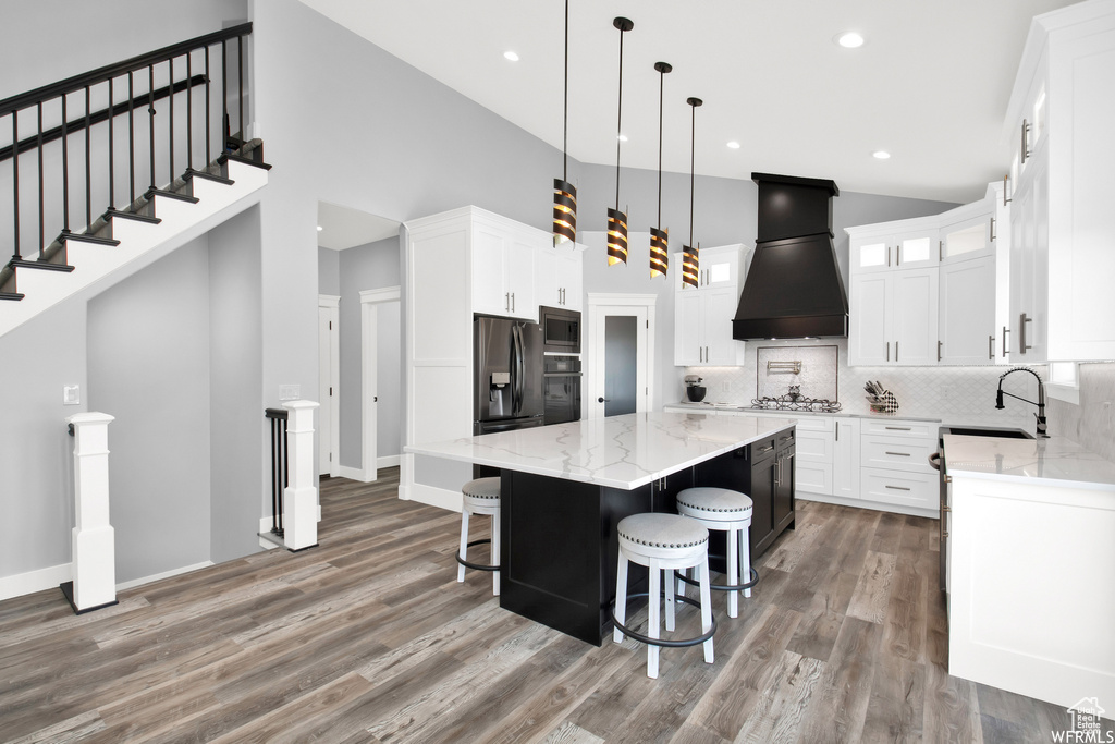 Kitchen featuring backsplash, premium range hood, a kitchen island, hardwood / wood-style flooring, and high vaulted ceiling