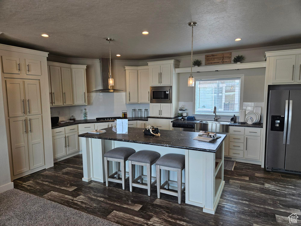 Kitchen with wall chimney range hood, a center island, pendant lighting, and stainless steel appliances