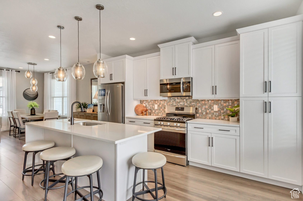 Kitchen featuring decorative light fixtures, stainless steel appliances, sink, a center island with sink, and light hardwood / wood-style floors