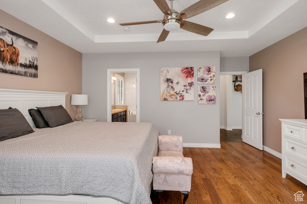 Bedroom with connected bathroom, wood-type flooring, ceiling fan, and a tray ceiling