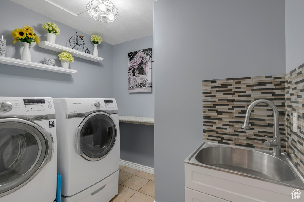 Washroom with light tile patterned flooring, washing machine and clothes dryer, and sink