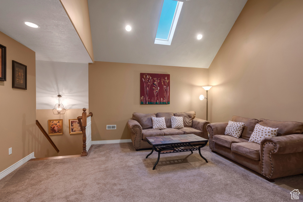 Carpeted living room featuring vaulted ceiling with skylight and a chandelier