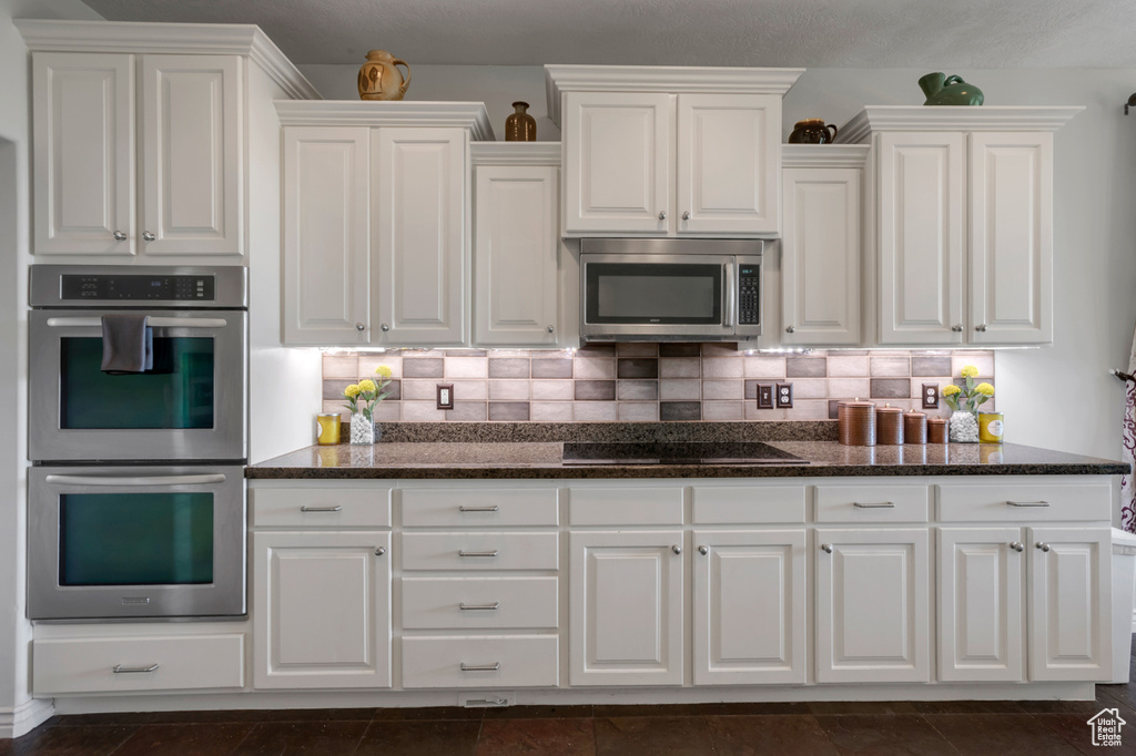 Kitchen with appliances with stainless steel finishes, white cabinetry, decorative backsplash, and dark stone counters