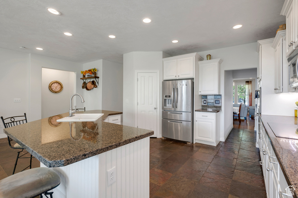 Kitchen with dark stone counters, white cabinetry, sink, a center island with sink, and appliances with stainless steel finishes