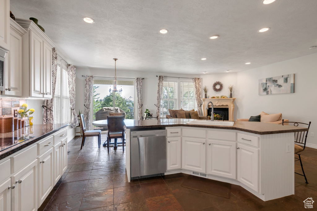 Kitchen with white cabinetry, dark tile patterned flooring, sink, dishwasher, and a kitchen breakfast bar