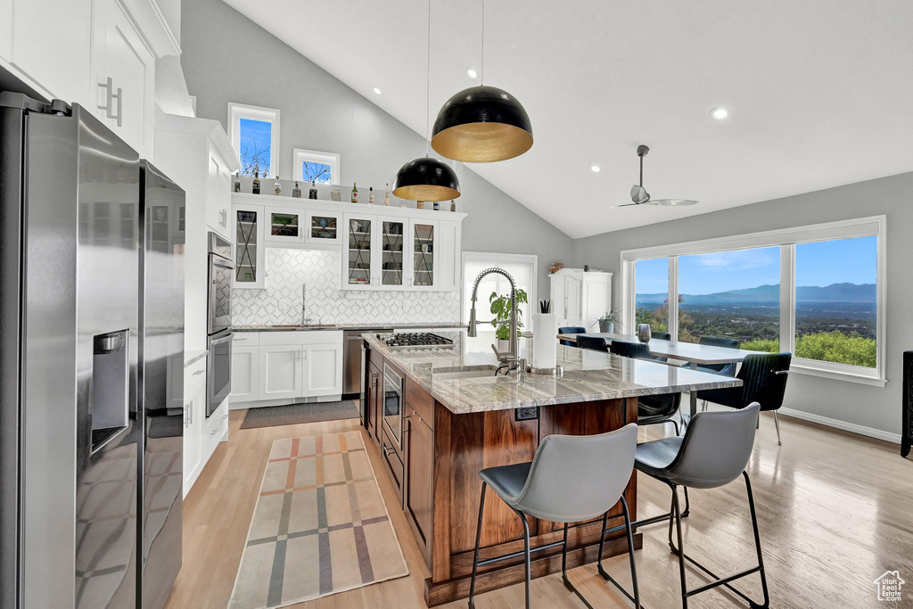 Kitchen featuring white cabinetry, refrigerator, backsplash, light hardwood / wood-style floors, and a center island with sink