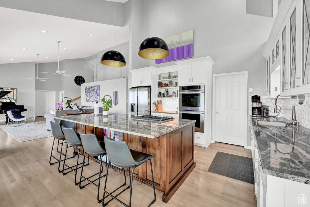 Kitchen with appliances with stainless steel finishes, light hardwood / wood-style flooring, stone countertops, white cabinetry, and a towering ceiling