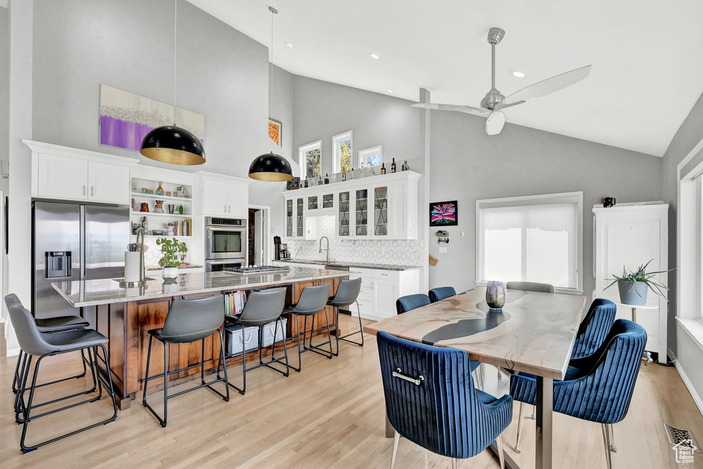 Dining space with sink, light hardwood / wood-style flooring, ceiling fan, and high vaulted ceiling