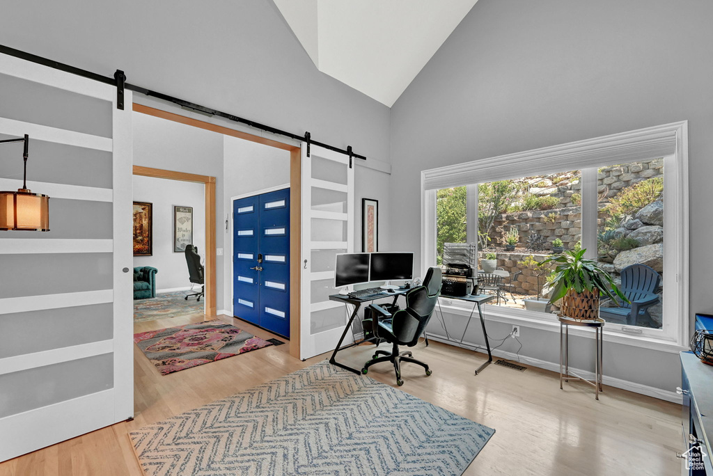 Office featuring high vaulted ceiling, light hardwood / wood-style flooring, and a barn door