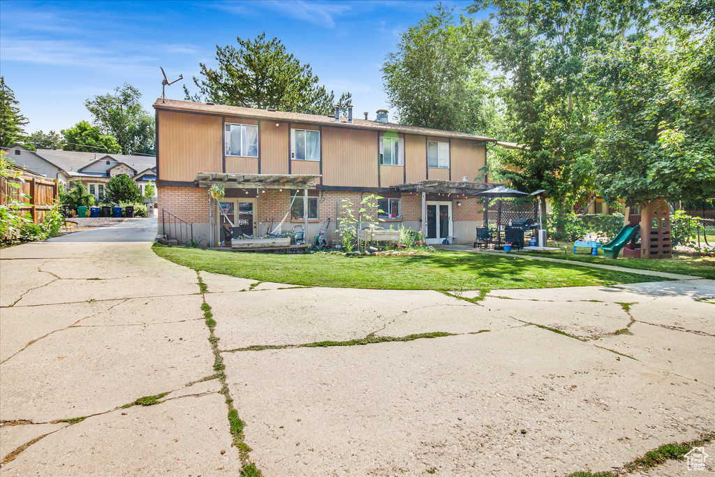 Rear view of house featuring a pergola, a yard, and a playground