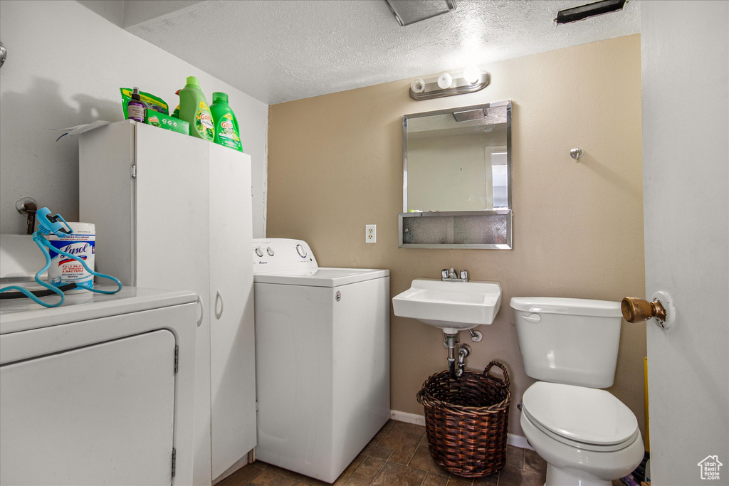 Laundry area with dark tile patterned floors, washer and clothes dryer, sink, and a textured ceiling