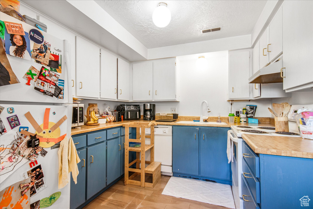 Kitchen featuring white appliances, a textured ceiling, blue cabinets, custom exhaust hood, and sink