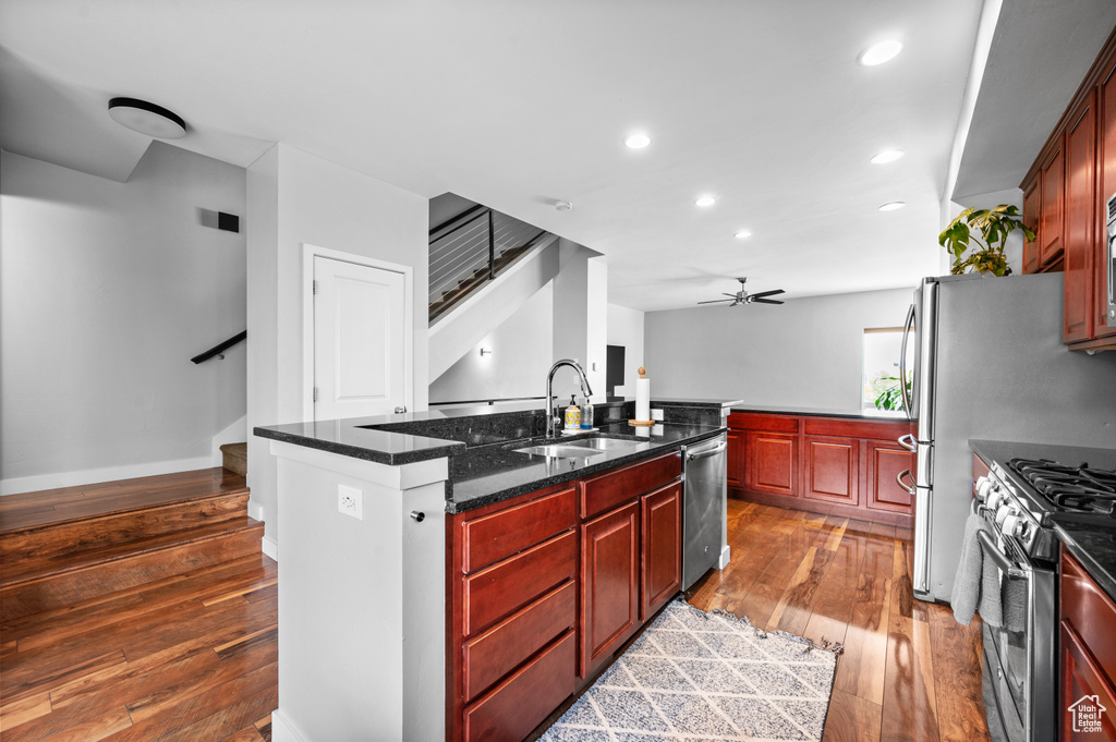 Kitchen with ceiling fan, stainless steel appliances, hardwood / wood-style floors, sink, and a center island with sink