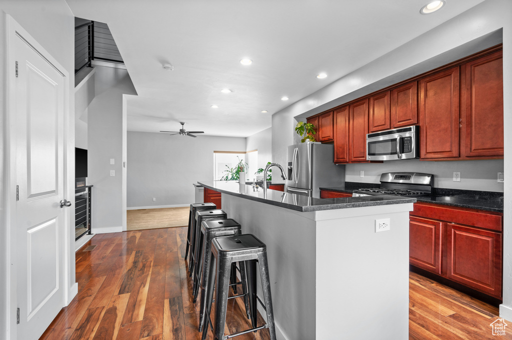 Kitchen with a breakfast bar area, stainless steel appliances, a kitchen island with sink, dark hardwood / wood-style flooring, and ceiling fan