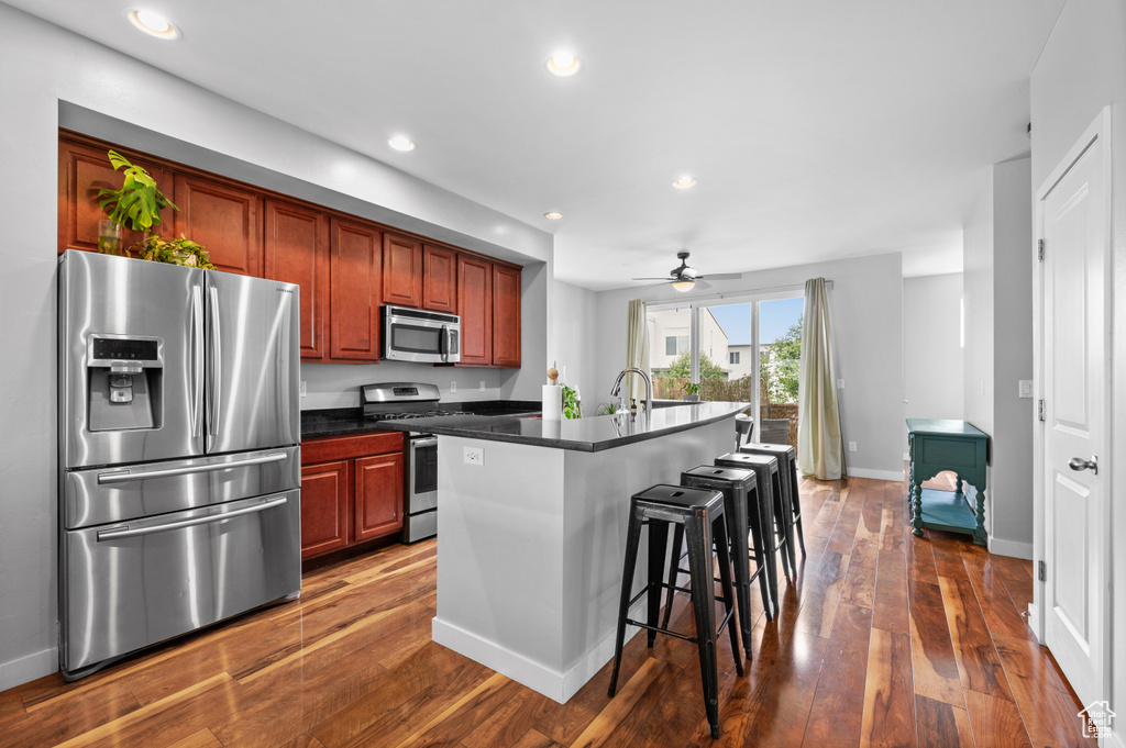 Kitchen featuring a kitchen island with sink, dark wood-type flooring, appliances with stainless steel finishes, and ceiling fan