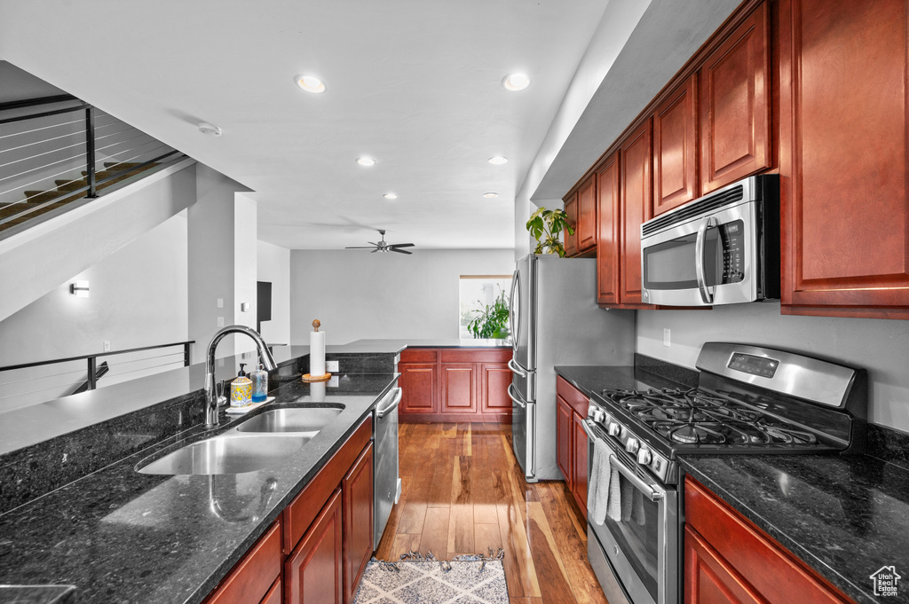 Kitchen with appliances with stainless steel finishes, dark stone counters, sink, light hardwood / wood-style floors, and ceiling fan