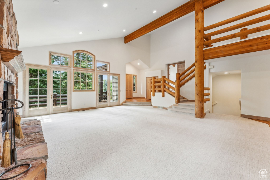 Carpeted living room featuring a fireplace, beamed ceiling, french doors, and high vaulted ceiling