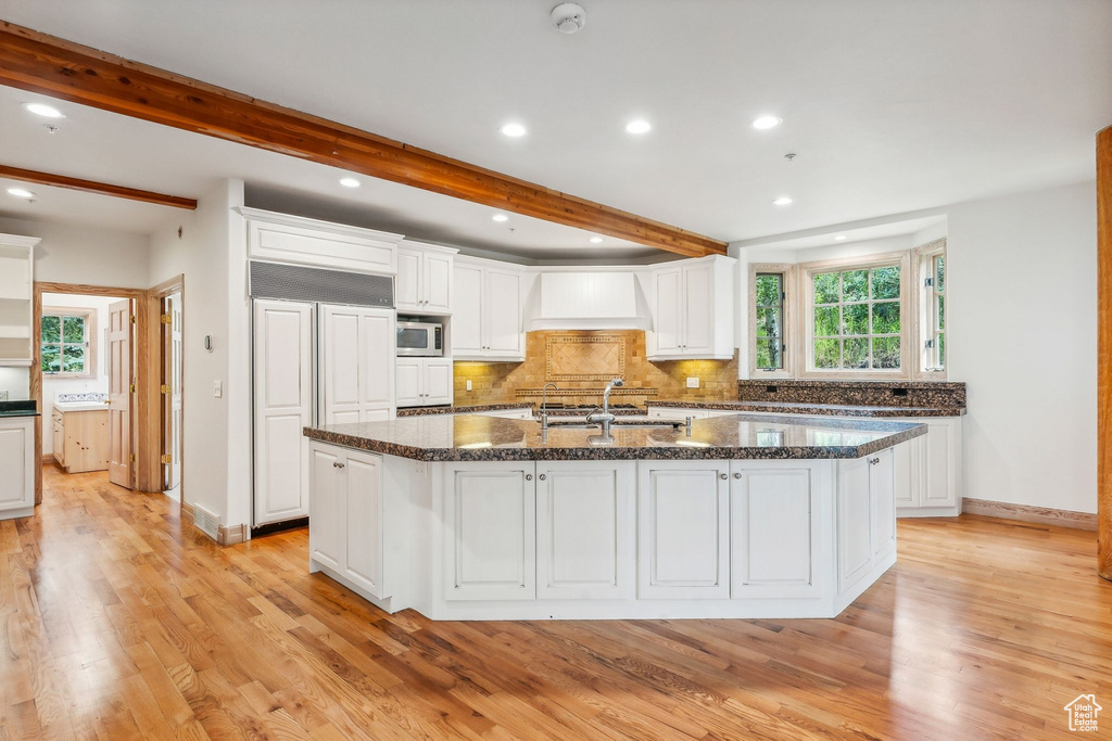 Kitchen featuring built in appliances, white cabinetry, light wood-type flooring, and a kitchen island with sink