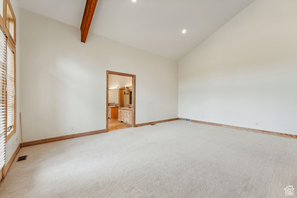 Carpeted spare room with high vaulted ceiling and beam ceiling