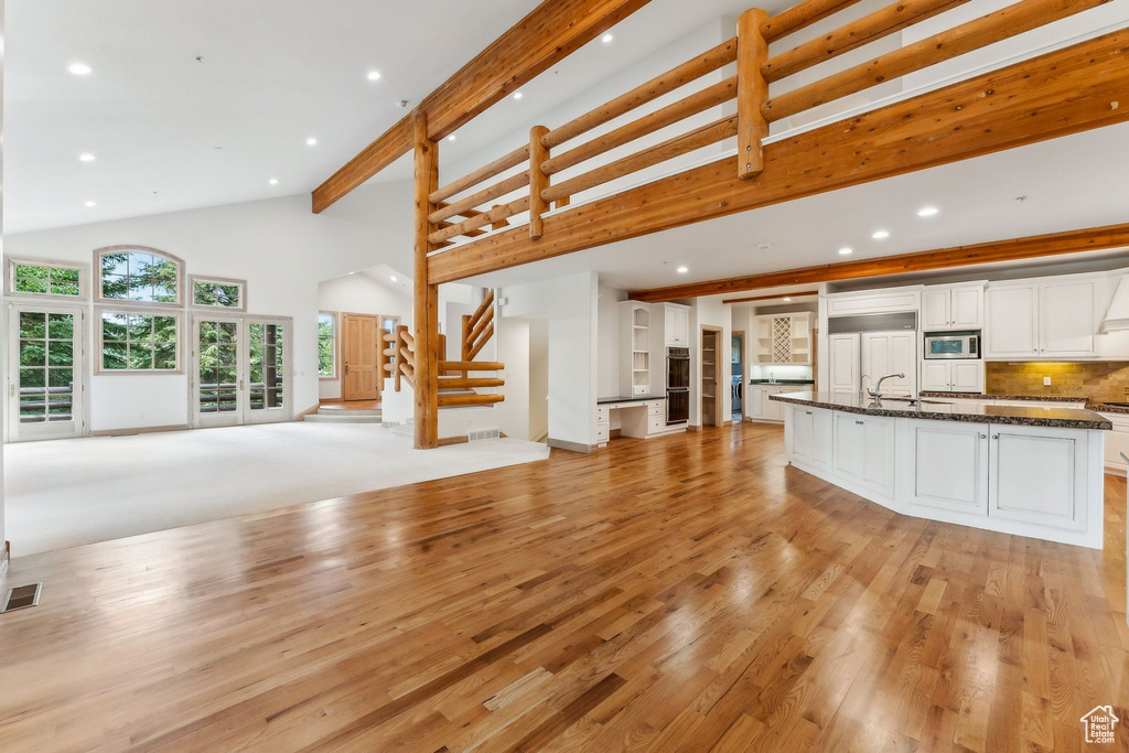 Unfurnished living room featuring sink, light carpet, and high vaulted ceiling