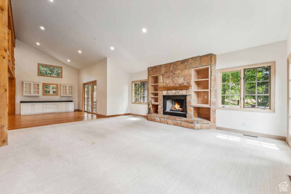 Unfurnished living room featuring light hardwood / wood-style flooring, a stone fireplace, and high vaulted ceiling