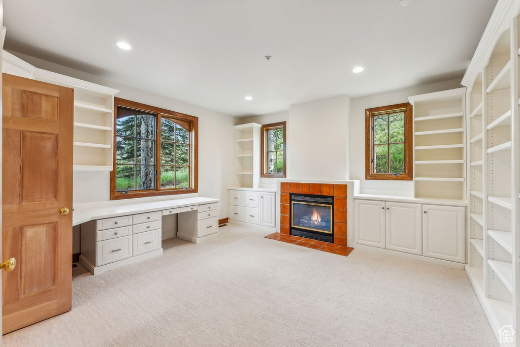 Unfurnished office with a tiled fireplace, light carpet, built in desk, and a healthy amount of sunlight