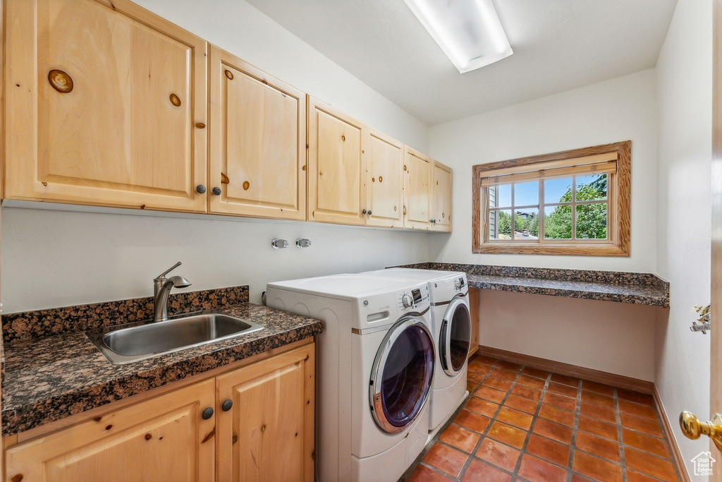 Clothes washing area with sink, dark tile patterned flooring, independent washer and dryer, and cabinets