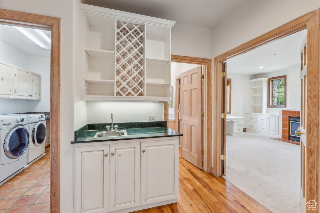 Kitchen with white cabinetry, sink, washing machine and dryer, and light colored carpet