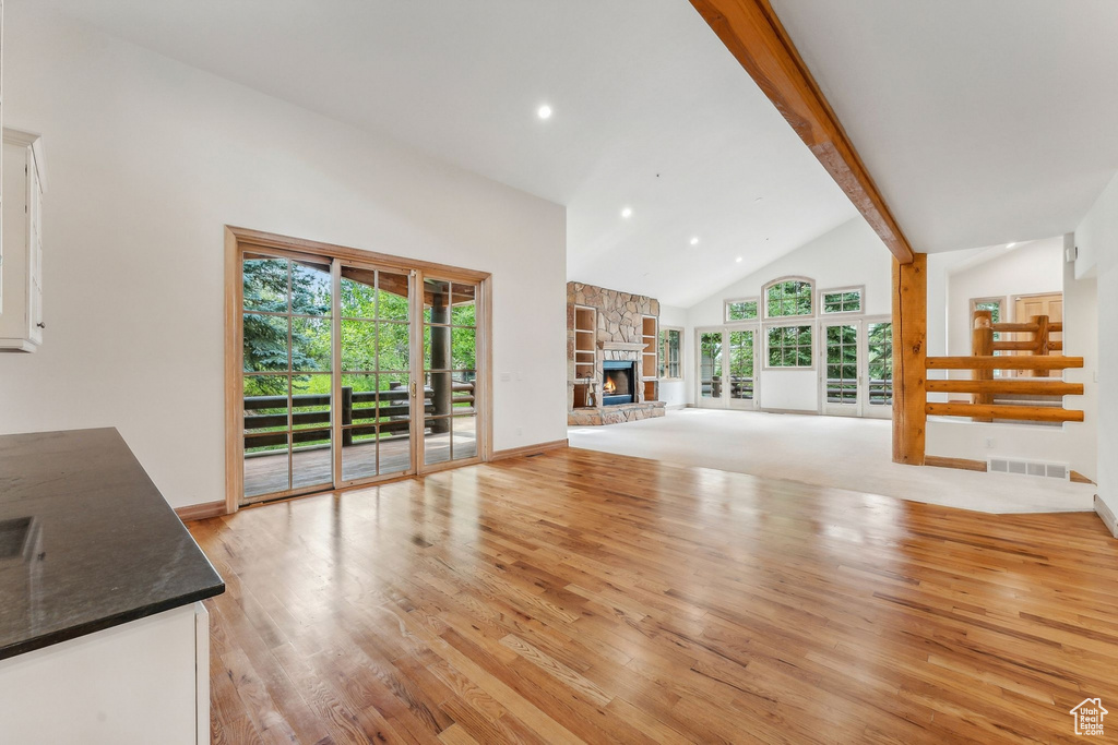 Unfurnished living room featuring a fireplace, beam ceiling, a wealth of natural light, and light colored carpet