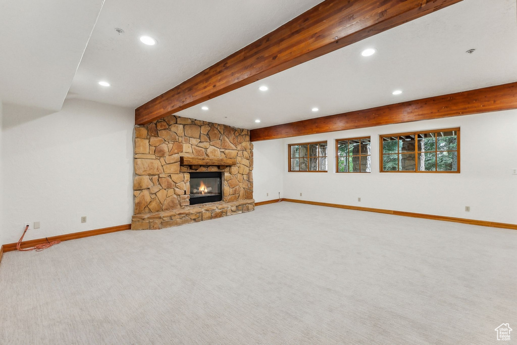 Unfurnished living room featuring carpet floors, a stone fireplace, and beam ceiling