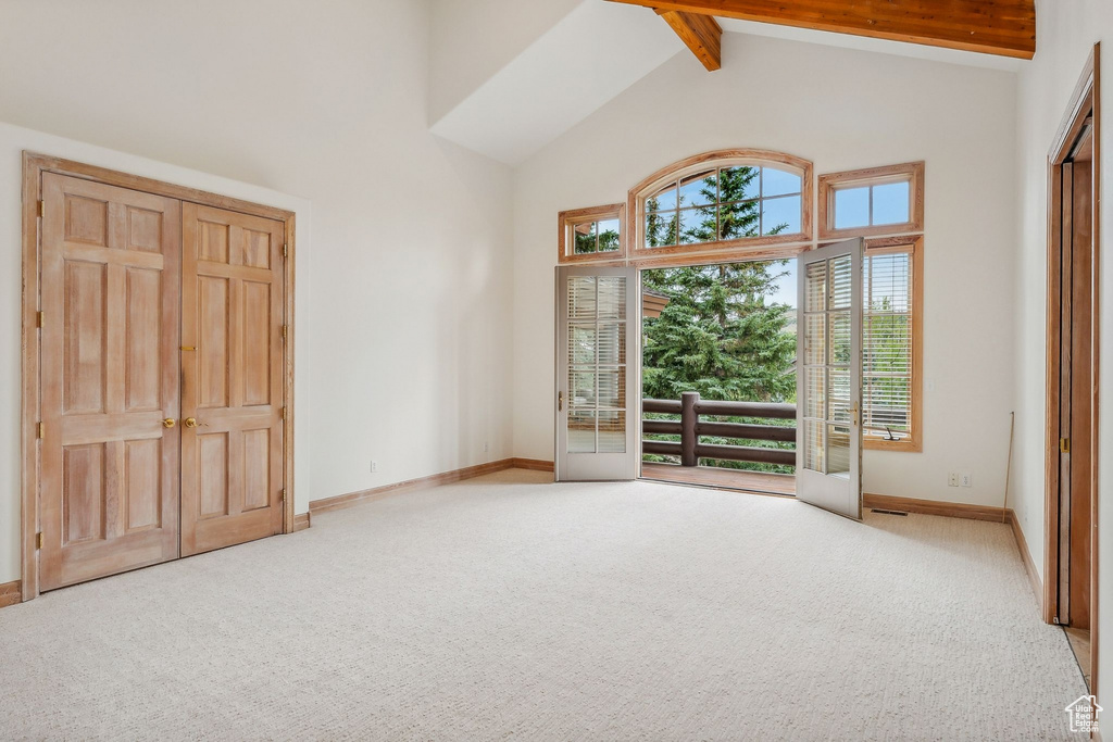 Unfurnished room featuring beamed ceiling, light carpet, and high vaulted ceiling