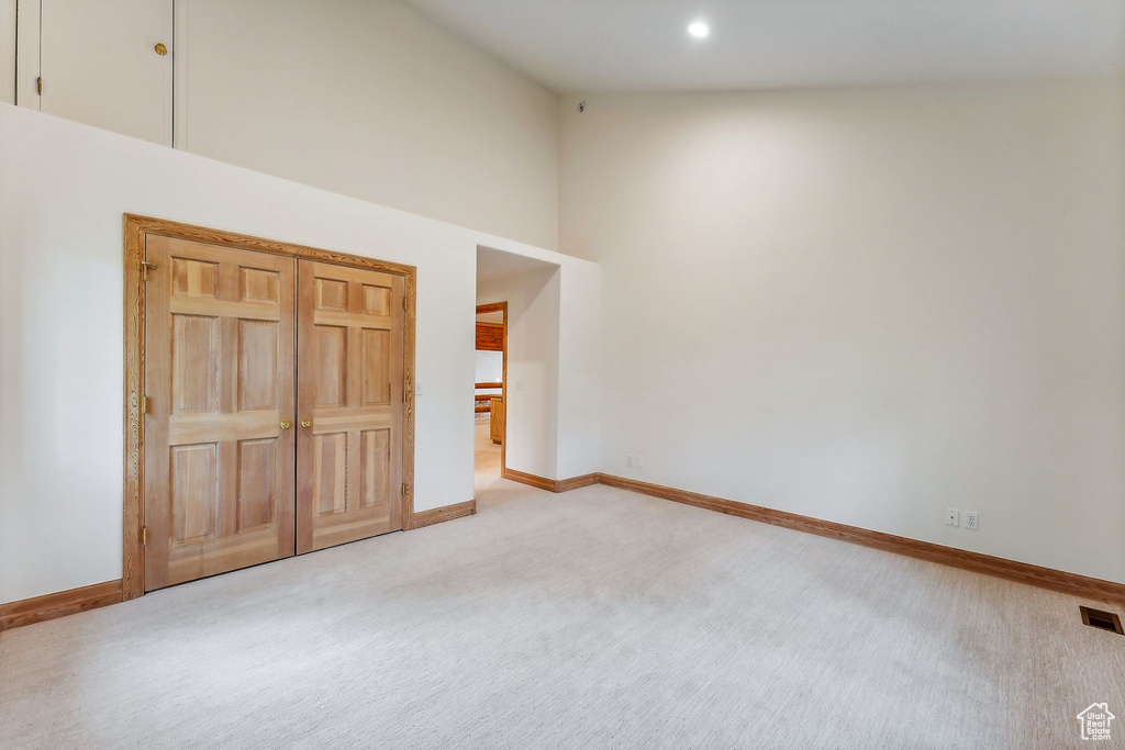 Unfurnished bedroom featuring high vaulted ceiling, a closet, and light colored carpet