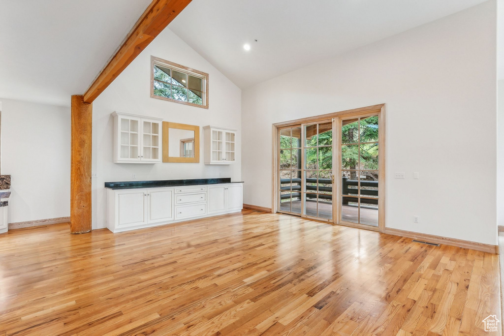 Unfurnished living room featuring light hardwood / wood-style flooring, beam ceiling, and high vaulted ceiling