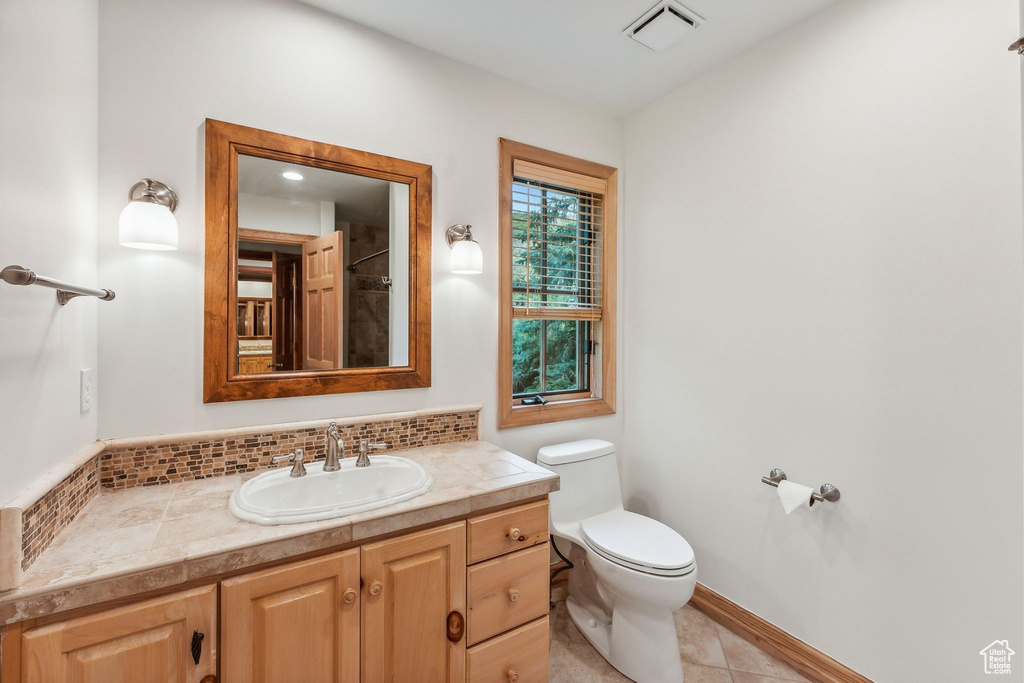 Bathroom with vanity, decorative backsplash, tile patterned flooring, and toilet