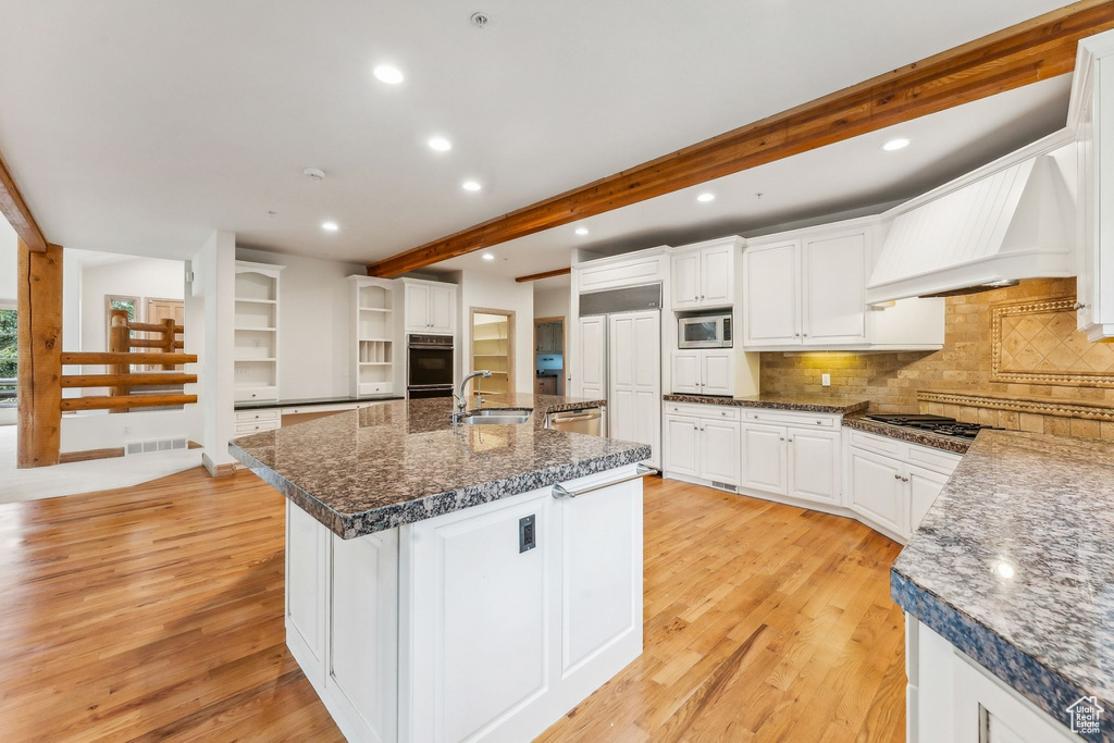 Kitchen featuring white cabinetry, stainless steel appliances, premium range hood, and light hardwood / wood-style flooring