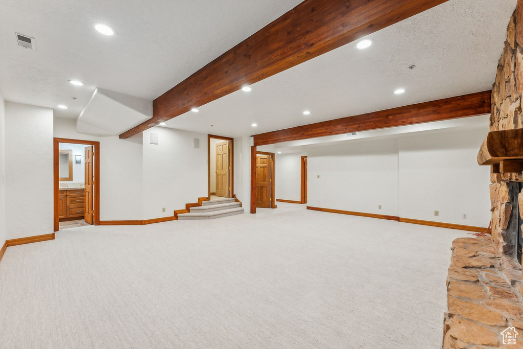 Basement featuring a stone fireplace, light colored carpet, and a textured ceiling