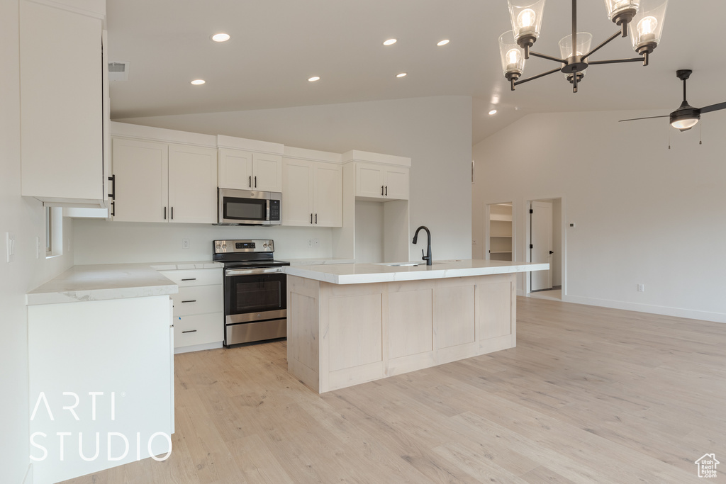 Kitchen with stainless steel appliances, ceiling fan with notable chandelier, light hardwood / wood-style flooring, and a kitchen island with sink